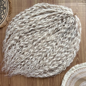 May include: A bundle of long, white, curly hair extensions. The hair is arranged in a loose, wavy pile.