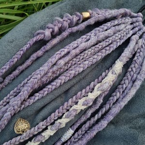May include: A set of lavender and white braided hair extensions. The extensions are made of a soft, textured material and are perfect for adding length and volume to your hair.