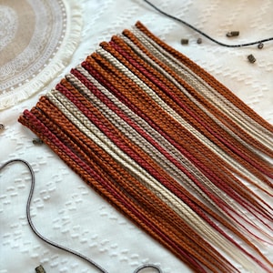 Op de afbeelding: Een set van 20 voorgevlochten haarextensies in een mix van bruin, rood en blond. De extensies zijn gemaakt van synthetisch haar en zijn klaar om te worden geïnstalleerd.