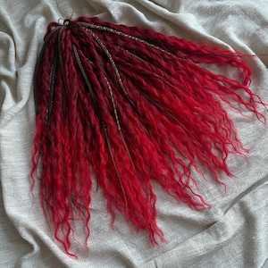 Könnte beinhalten: Ein Bündel leuchtend roter Dreadlocks mit welliger Textur. Die Dreadlocks haben einen Farbverlauf, der von einem dunkleren Farbton an den Wurzeln zu einem leuchtenden Rot an den Enden übergeht. Einige Strähnen sind mit braunen und goldenen Akzenten geflochten.