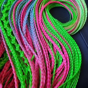 May include: A close-up of a bundle of brightly colored synthetic hair extensions. The hair is braided and comes in shades of pink, green, and blue.