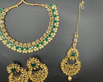 May include: A gold-coloured jewellery set comprising a necklace, earrings, and a headpiece. The necklace and earrings feature green teardrop-shaped stones and small pearls. The headpiece has a central green stone and a dangling pearl.