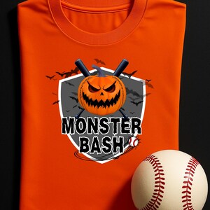 Puede incluir: Camiseta naranja con un gráfico de "Monster Bash" con una calabaza de béisbol y bates. Una pelota de béisbol con costuras rojas está en primer plano. La camiseta está doblada cuidadosamente.