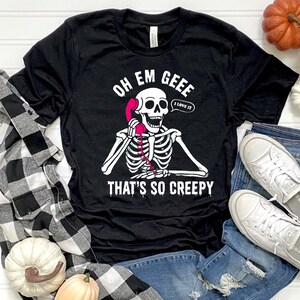May include: Black t-shirt with a white skeleton graphic holding a pink telephone. The text on the shirt reads "OH EM GEEE THAT'S SO CREEPY" with a speech bubble saying "I LOVE IT".