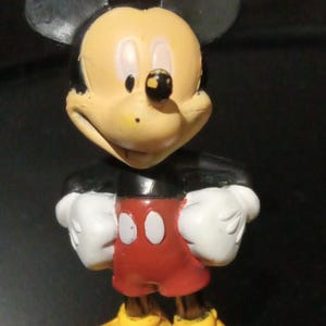 Może przedstawiać: Czarno-ż&oacute;łta figurka Myszki Miki w czerwono-białym stroju. Figurka jest wykonana z plastiku i ma kresk&oacute;wkowy styl.