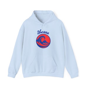 Può includere: Una felpa con cappuccio di colore azzurro chiaro con un logo rosso e blu che dice "Moana" e presenta un'onda in un cerchio.