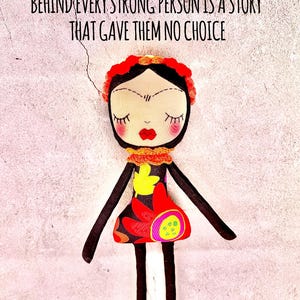May include: A colourful handmade doll with a black and white striped dress, red flowers, and yellow leaves. The doll has a black and white striped body, a red flower crown, and a black unibrow. The doll is against a white textured background with the text "Behind every strong person is a story that gave them no choice".