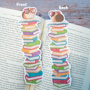 May include: Two colorful bookmarks, each featuring a stack of books topped with a guinea pig wearing glasses. The books are in various colors, and the bookmarks are set against a book page.