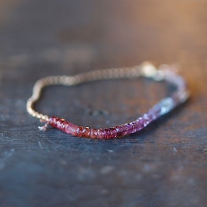 May include: A delicate gold chain bracelet with a gradient of pink, red, and blue gemstones.