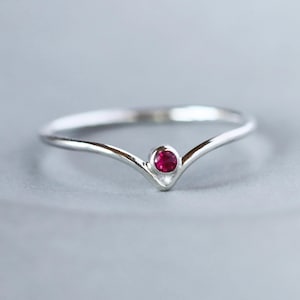 May include: A silver ring with a V-shaped band and a small, round, red gemstone in the center.