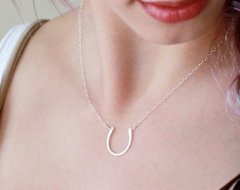 May include: A silver horseshoe pendant necklace on a silver chain. The necklace is worn by a person with purple hair.