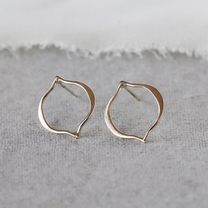 May include: A pair of silver stud earrings. Each earring features an open, teardrop-shaped design with a smooth, polished finish. The earrings are displayed on a gray surface, with a soft, white fabric in the background.