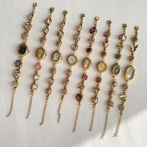 Pu&ograve; includere: Una collezione di otto braccialetti con ciondoli dorati con piccoli quadranti. Ogni braccialetto presenta un diverso design del quadrante ed &egrave; adornato con varie pietre preziose e ciondoli decorativi, tra cui fiori e farfalle.