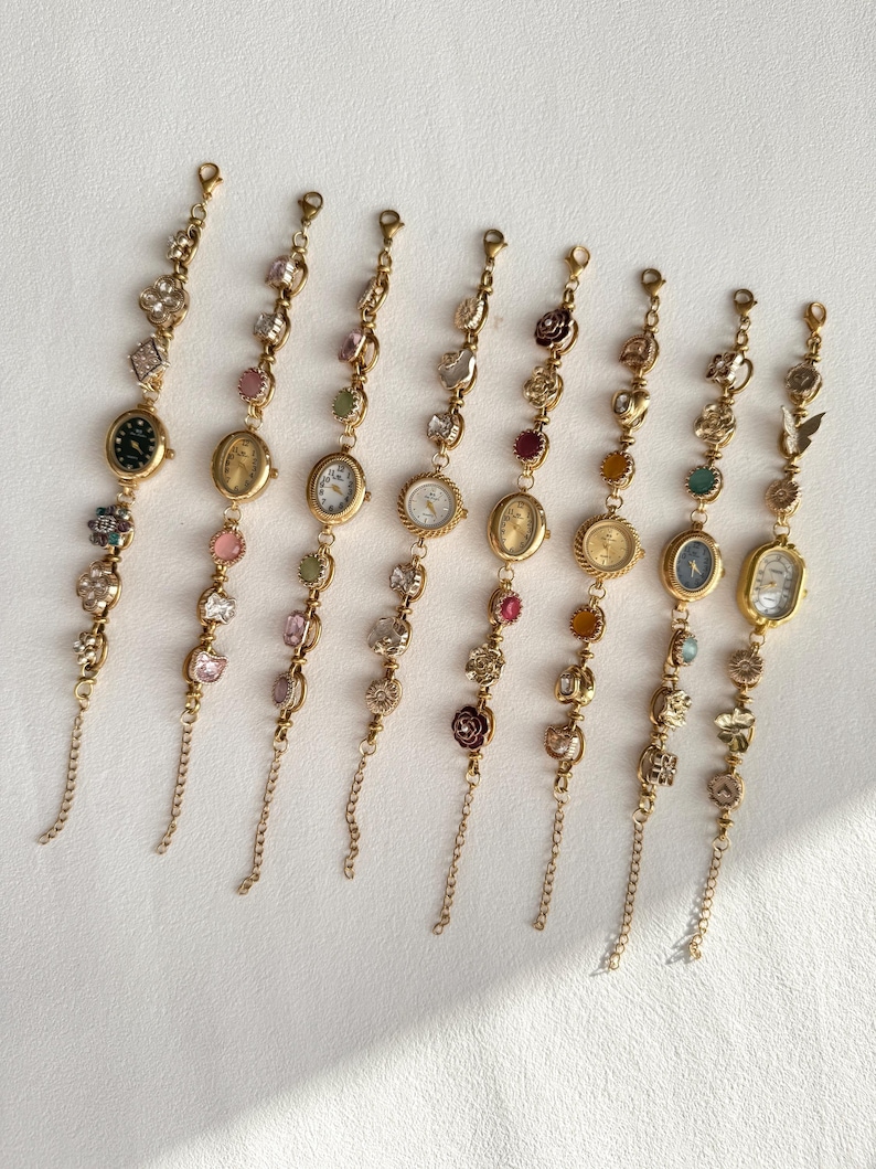 Pu&ograve; includere: Una collezione di otto braccialetti con ciondoli dorati con piccoli quadranti. Ogni braccialetto presenta un diverso design del quadrante ed &egrave; adornato con varie pietre preziose e ciondoli decorativi, tra cui fiori e farfalle.