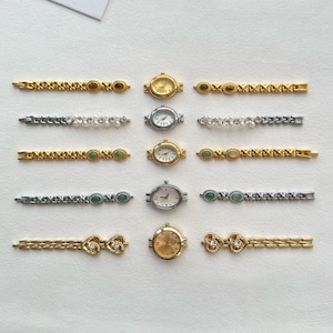 May include: An assortment of small, decorative wristwatches and watch bands. The watches have gold and silver-toned cases with white faces. The bands are gold and silver-toned, some with decorative stones and pearls. The watches and bands are arranged on a white surface.