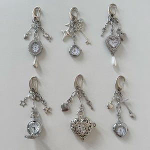 Può includere: Sei portachiavi argentati con mini quadranti e ciondoli decorativi. I ciondoli includono stelle, chiavi, cuori e croci. Ogni portachiavi ha un fermaglio per l'attacco.