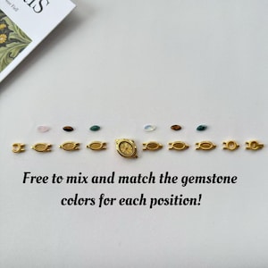 May include: A collection of gold-toned watch components and gemstones arranged on a white surface. The gemstones are in various colors, and the text reads, "Free to mix and match the gemstone colors for each position!"