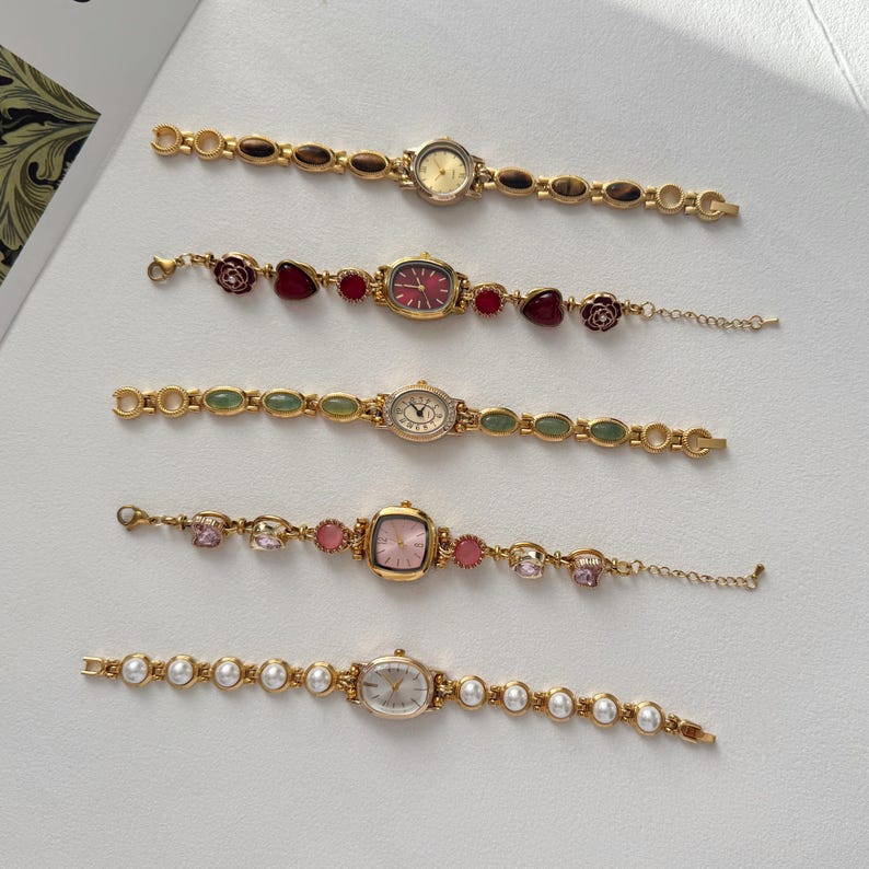 Puede incluir: Cinco relojes de pulsera dorados con diferentes formas de esfera y correas decorativas. Las correas presentan piedras preciosas, perlas y otros adornos. Las esferas son en tonos dorados, rosas y blancos.