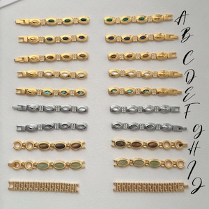 May include: A collection of gold and silver-toned bracelets with various gemstone and crystal embellishments. The bracelets feature oval and rectangular links, with a variety of colored stones including green, blue, and brown. Some bracelets have a classic link design.