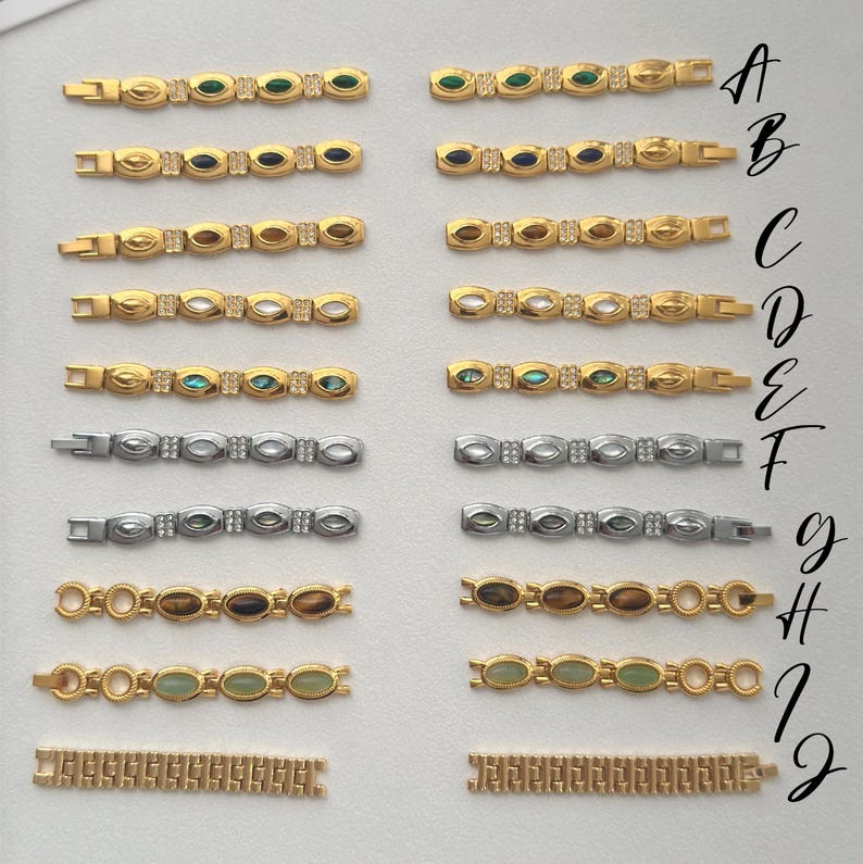 May include: A collection of gold and silver-toned bracelets with various gemstone and crystal embellishments. The bracelets feature oval and rectangular links, with a variety of colored stones including green, blue, and brown. Some bracelets have a classic link design.