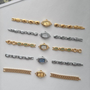 May include: An assortment of vintage women's watches and watch bands in gold and silver tones. The watches have rectangular faces with various dial colors, including gold, white, and blue. The bands feature decorative links with gemstones.