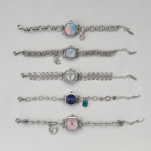 May include: Five silver-toned wristwatches with square faces and various colored dials, including pink, blue, and white. Each watch has a unique chain-link bracelet with decorative charms. The watches are displayed on a white surface.