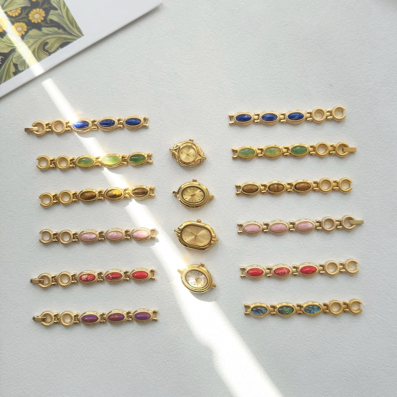 K&ouml;nnte beinhalten: Eine Sammlung goldfarbener Uhrenarmb&auml;nder und kleiner Uhren mit verschiedenfarbigen, oval geformten Steinen. Die Armb&auml;nder weisen blaue, gr&uuml;ne, braune, rosa, rote und violette Steine auf. Die Uhren haben goldene Zifferbl&auml;tter.