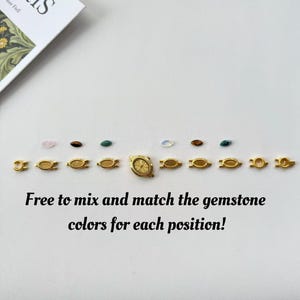 K&ouml;nnte beinhalten: Eine Sammlung goldfarbener Uhrenkomponenten und Edelsteine in verschiedenen Farben. Die Komponenten umfassen Verschl&uuml;sse und ein Zifferblatt. Der Text "Free to mix and match the gemstone colors for each position!" ist ebenfalls sichtbar.