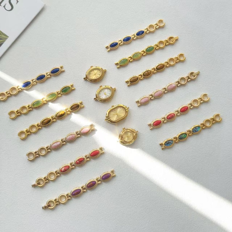 K&ouml;nnte beinhalten: Goldfarbene Zifferbl&auml;tter und passende Armbandglieder mit farbigen, oval geformten Steinen. Die Zifferbl&auml;tter haben eine klassische ovale Form. Die Armbandglieder weisen blaue, gr&uuml;ne, braune, rosa, rote und violette Steine auf.