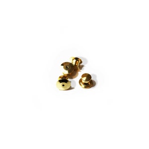 May include: Four gold-colored metal pin backs for attaching badges or other items to clothing.
