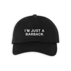 May include: Black baseball cap featuring the white text "I'M JUST A BARBACK". The cap has a curved peak and a rounded crown. A casual accessory for everyday wear.