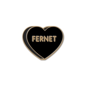 May include: A black heart-shaped pin with the word "FERNET" in gold lettering. The pin has a gold border and a black interior, set against a white background. This pin is a stylish accessory.