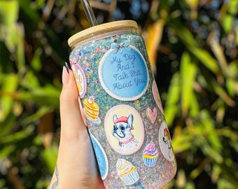 May include: A glitter-covered glass tumbler with a bamboo lid and a clear straw. The tumbler is decorated with cartoon images of a dog, cupcakes, and pancakes. Text on the tumbler reads "My Dog And I Talk Shit About You."