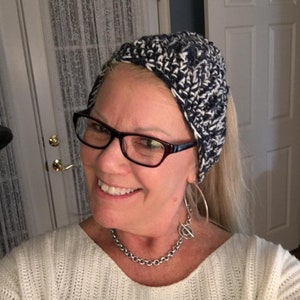 May include: A woman wearing a white sweater, a black and white crocheted headband, and a silver chain necklace with a toggle clasp.