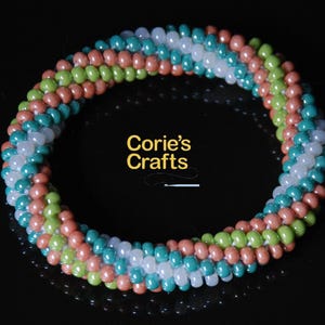 Puede incluir: Un brazalete de cuentas multicolores con un diseño en espiral. El brazalete está hecho con cuentas blancas, verde azulado, verdes y melocotón.