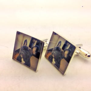 May include: A pair of silver cufflinks with a square image of a French bulldog on each. The dog is black and white and has its tongue sticking out.