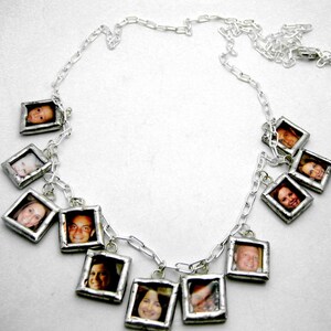 Op de afbeelding: Een zilveren ketting met meerdere kleine zilveren fotolijstjes die eraan hangen. Elk lijstje bevat een andere foto van een gezicht.