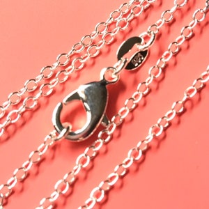 May include: A silver chain necklace with a lobster clasp. The chain is made of small, round links. The chain is lying on a pink surface.