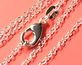 May include: A silver chain necklace with a lobster clasp. The chain is made of small, round links. The chain is lying on a pink surface.