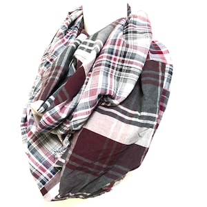 Puede incluir: Una bufanda infinita de cuadros grises, blancos, burdeos y azul marino. La bufanda está hecha de un tejido suave y tejido.