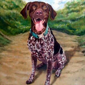 May include: A brown and white spotted dog with a teal collar sits on a dirt path. The dog has its tongue sticking out and is smiling. The dog is in front of a green grassy background.