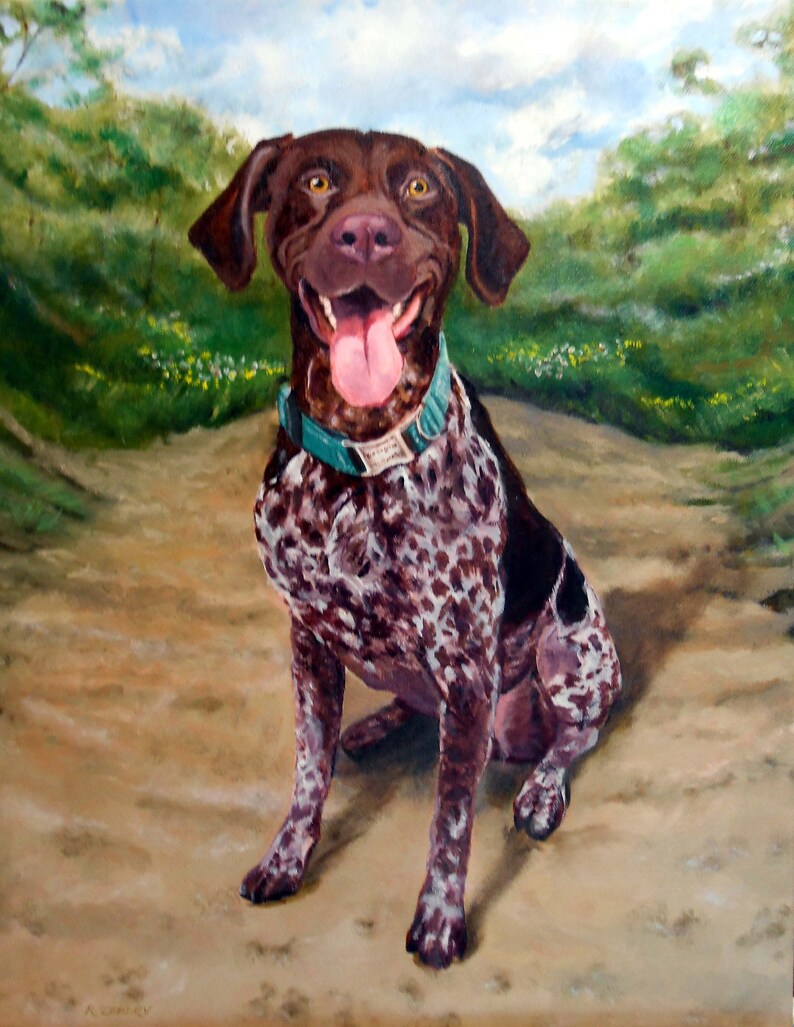 May include: A brown and white spotted dog with a teal collar sits on a dirt path. The dog has its tongue sticking out and is smiling. The dog is in front of a green grassy background.