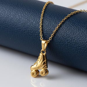 Op de afbeelding: Een goudkleurige ketting met een hanger in de vorm van een rolschaats. De hanger is een gedetailleerde miniatuur van een klassieke rolschaats, compleet met wielen en veters. De ketting is ook goudkleurig en ligt op een blauw oppervlak.