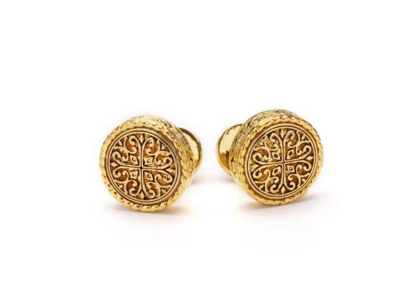 May include: A pair of gold cufflinks with a circular design featuring an intricate, engraved floral pattern.