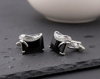 May include: A pair of rectangular silver cufflinks featuring a large, polished black stone set in the center. Each cufflink is accented with a curved silver band embedded with small, clear, sparkling stones along the top edge of the black stone.