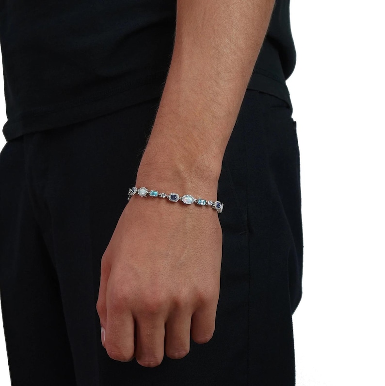 May include: A silver-toned link bracelet featuring alternating oval-shaped white opalescent stones and rectangular blue gemstones. The bracelet is secured with a metal clasp and displays a series of small, clear, sparkling stones set between each larger gem.