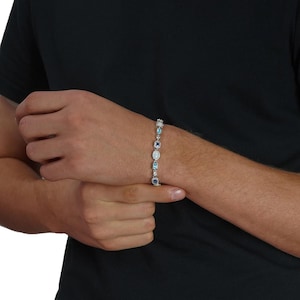May include: A silver-toned link bracelet featuring alternating oval and rectangular gemstones in shades of light blue, dark blue, and iridescent white. The stones are set in metallic frames and connected by small silver-toned circular links.