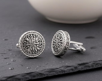 May include: A pair of round silver cufflinks featuring an intricate, symmetrical filigree pattern on the face and a twisted rope-style border. The metal has a polished finish with darkened recessed areas to highlight the detailed scrollwork design.