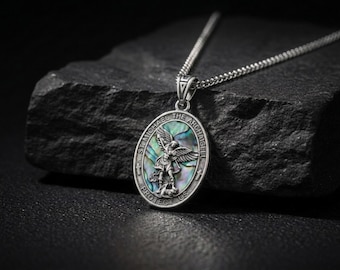 Può includere: Un ciondolo ovale in argento su catenina con un rilievo di San Michele Arcangelo su un intarsio in conchiglia di abalone iridescente. Il bordo reca l'iscrizione ST. MICHAEL THE ARCHANGEL PROTECT US, accentuata da due piccole croci.