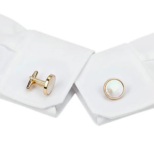 May include: Gold-toned cufflinks with a mother-of-pearl inlay. One cufflink is a bar style, and the other is a round, button style. The cufflinks are displayed on a white dress shirt cuff.